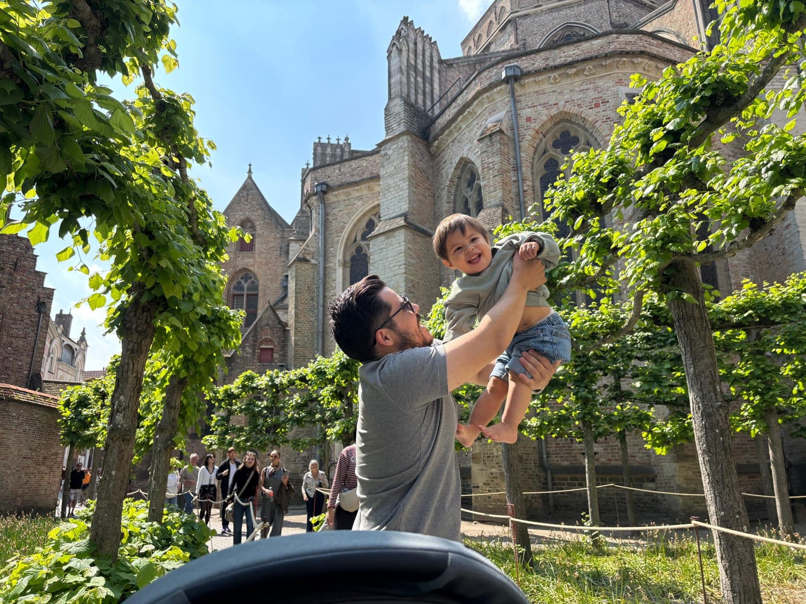 Yeriel lifting his laughing toddler outside on a sunny day.